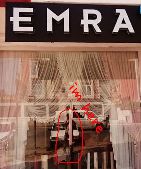 A business representative in front of Emra Home Fashion is visible through the shop window with lace curtains.