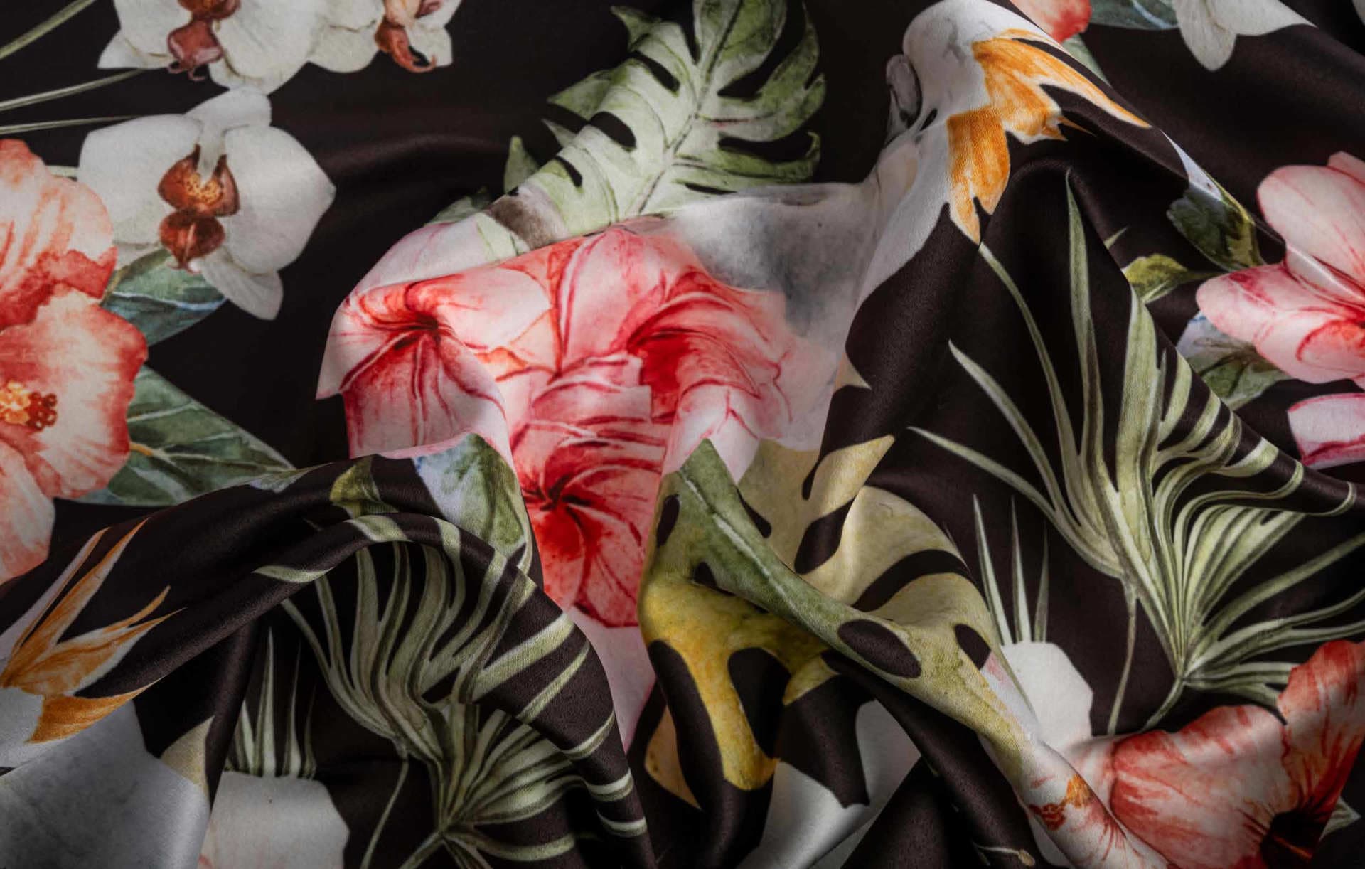 Close-up of draped fabric with a vibrant floral and botanical print featuring pink and orange flowers and green leaves on a dark background.