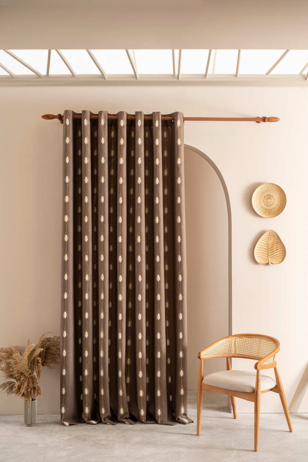 A brown curtain with a repeating light-colored pattern hangs on a rod in a room with a chair and decor.