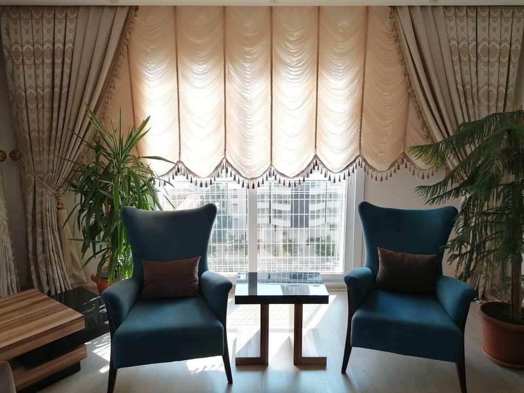 Two turquoise wingback armchairs and a small coffee table in front of elegant curtains