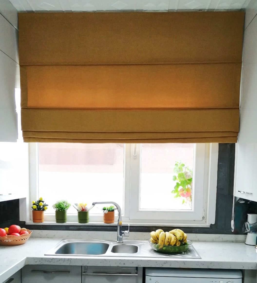 Kitchen counter with sink and plants under a window with a folded brown Roman blind