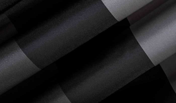 This fabric, a close-up of a material with alternating glossy and matte textures, in black and dark gray colors with large diagonal stripes (similar to plaid), appears wavy due to its draped positioning.