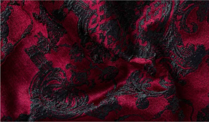 A luxurious upholstery fabric detail with a red background, embroidered with black baroque patterns, and a velvet texture.