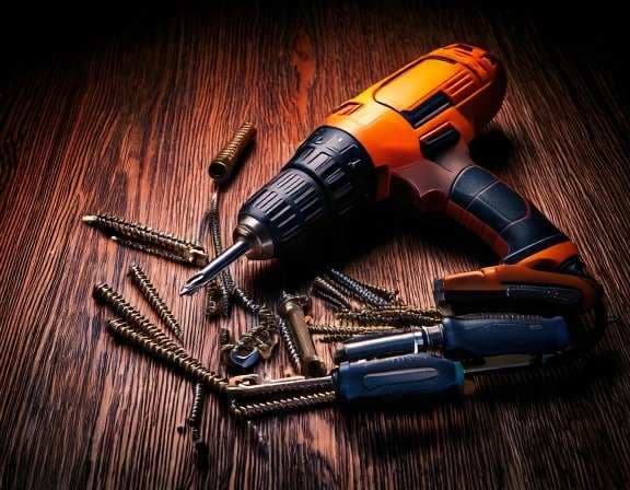 Orange and black cordless drill with screws and screwdrivers on wood.
